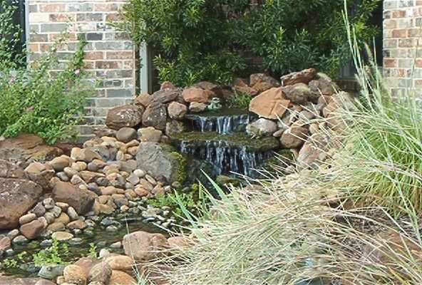 Stacked-stone waterfall spilling into a rock basin beside a brick wall