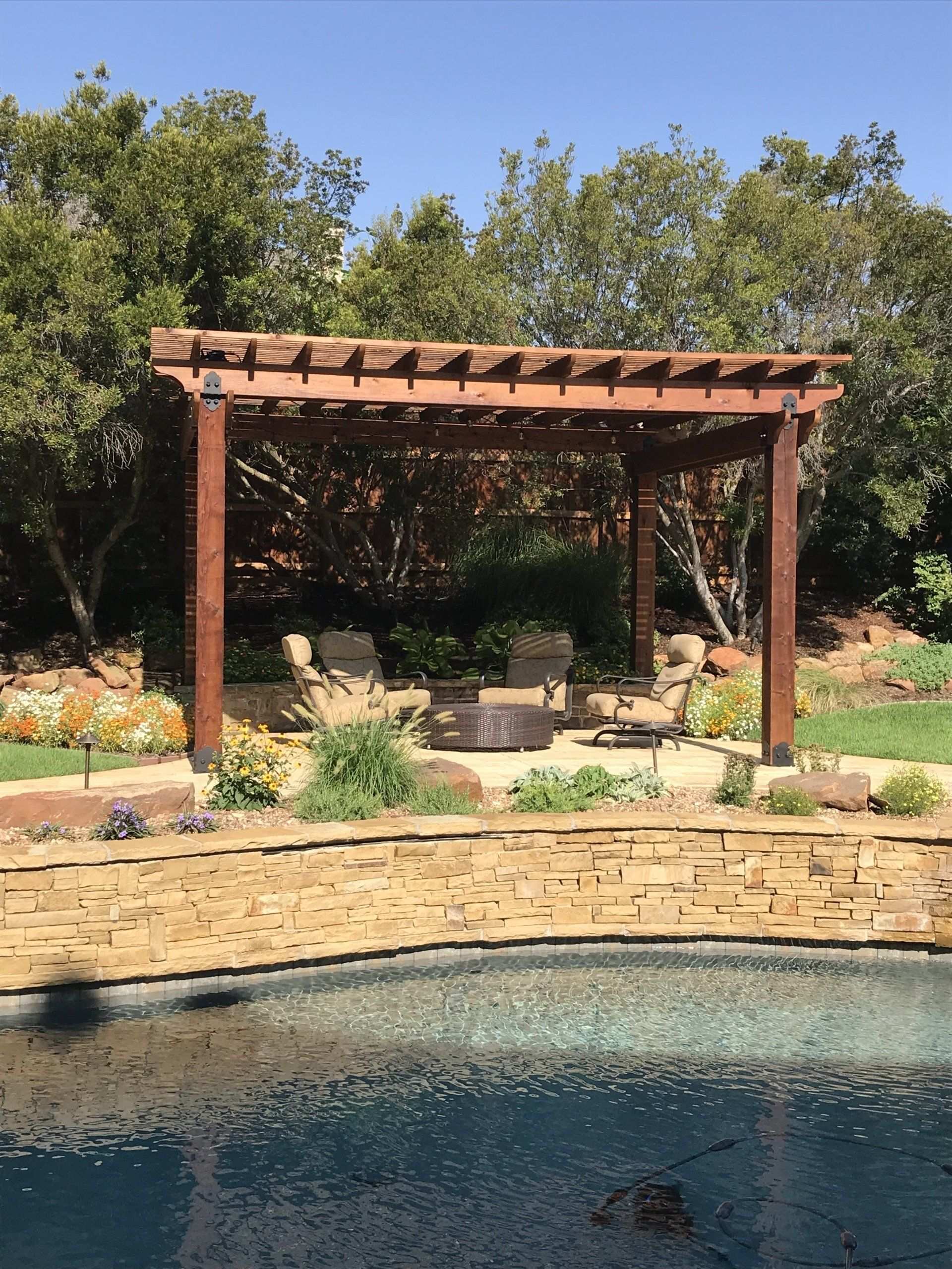 Cedar pergola over a poolside patio behind a stone retaining wall