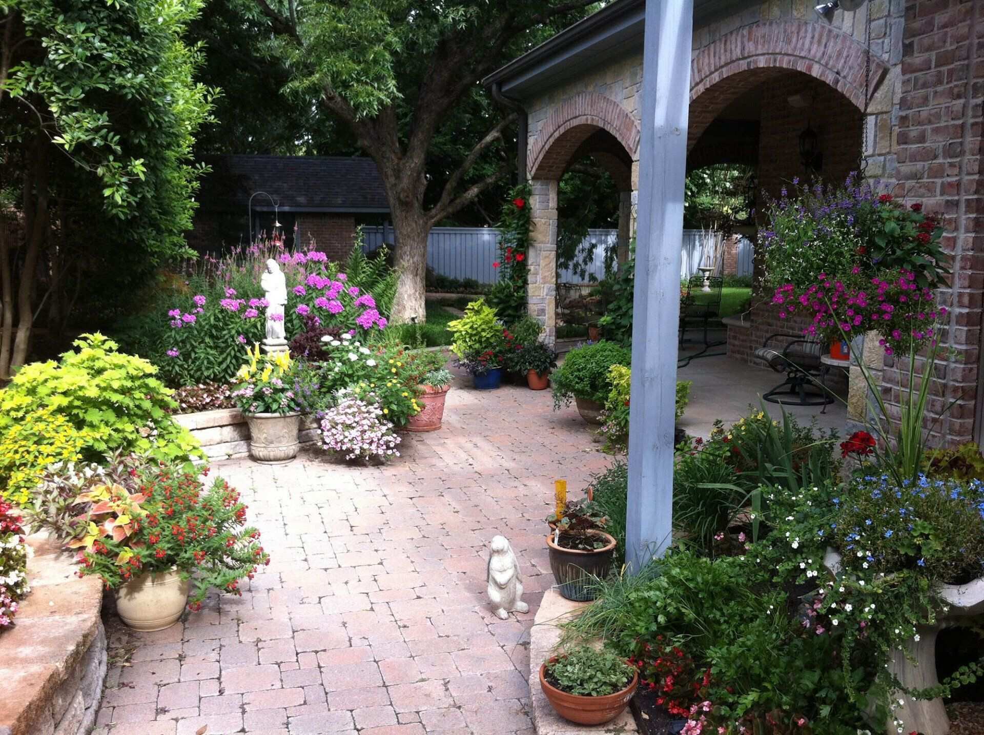 Brick courtyard patio lined with potted flowering plants under a covered arch