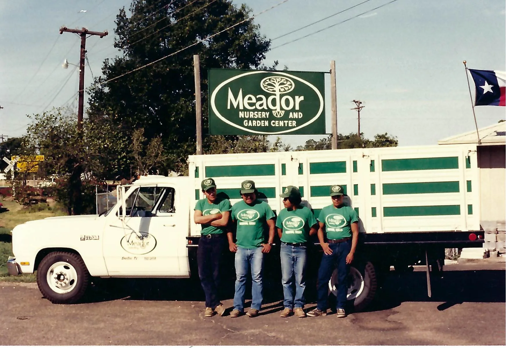 Four staff in Meador Nursery T-shirts and caps standing alongside a green-and-white Meador stake-bed truck, beneath the Meador Nursery and Garden Center sign