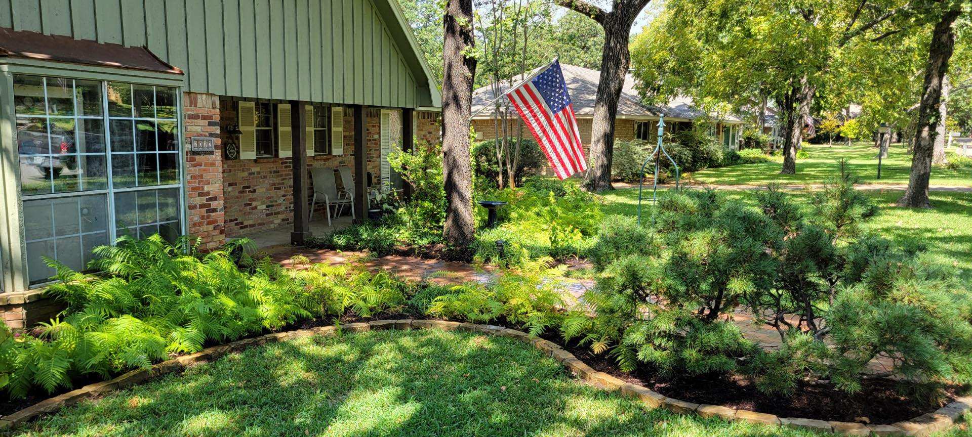 Front yard bed of clipped evergreens and perennials beside a green-sided house