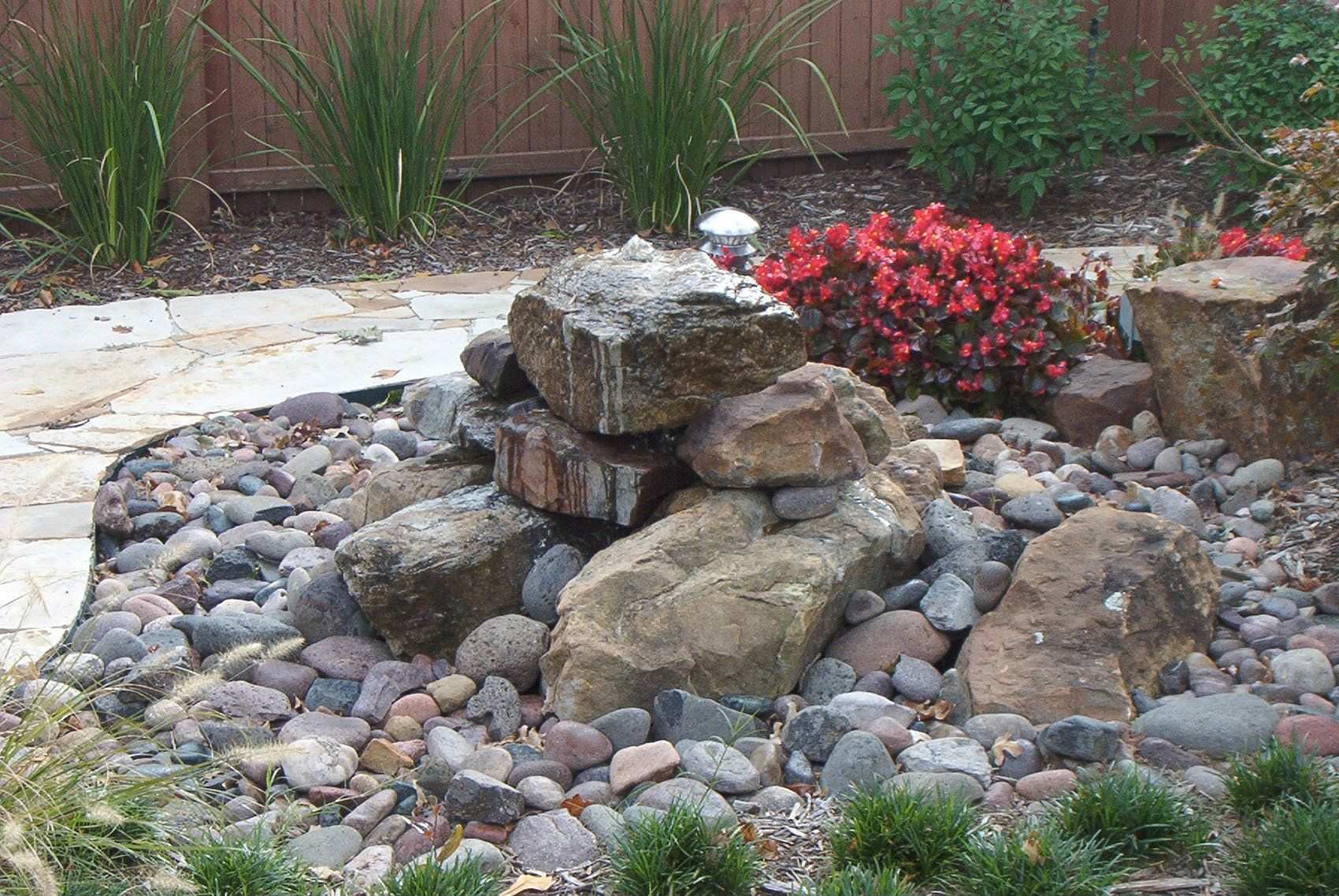 Rock waterfall feature built from boulders, planted with red flowers and ornamental grasses