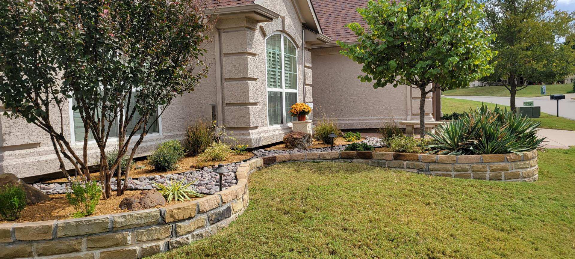 Stone-terraced planting bed with young trees in a front lawn
